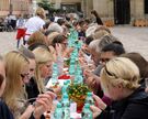 Menschen essen zusammen an einer langen Tafel auf dem Domhof bei einer Veranstaltung der Caritas.