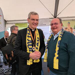 Bischof Dr. Heiner Wilmer SCJ und Diözesanratsvorsitzender Dr. Christian Heimann treffen sich am Bistumsstand auf dem Katholikentag 2026. 