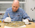 Restaurator Uwe Schuchardt säubert das vor ihm liegende Große Scheibenkreuz mit einem Pinsel. 