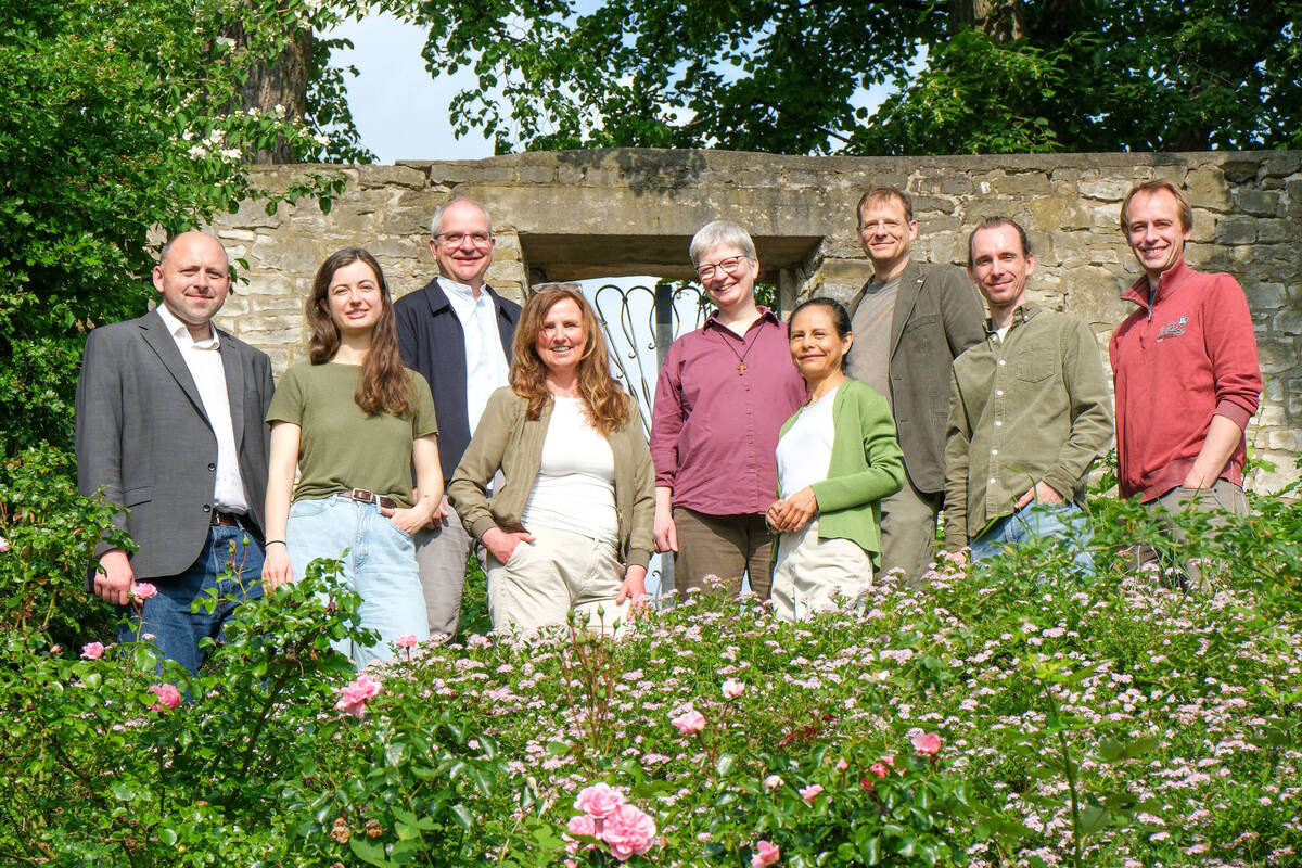 Foto des Umweltteams inmitten eines Gartens mit Rosen im Vordergrund, Bäumen und einer alten Mauer im Hintergrund