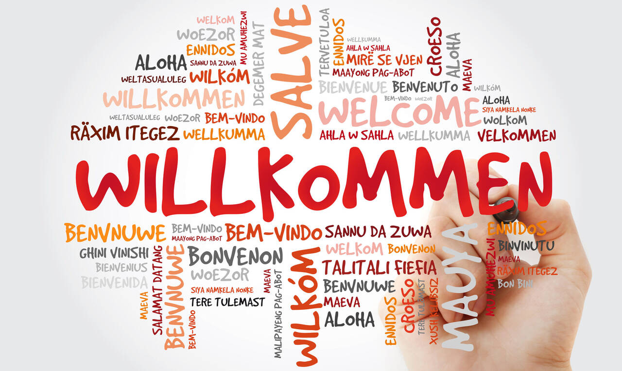 Willkommen - Wortwolke in verschiedenen Sprachen und einer Hand mit Stift