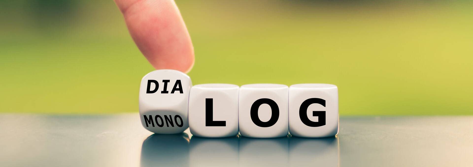 Symbolbild zum Interreligiösen Dialog: Hand dreht einen Würfel und ändert das Wort "Monolog" in "Dialog".