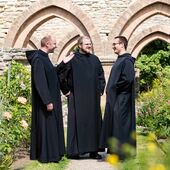 Drei Benediktinerbrüder in einer Klosteranlage.