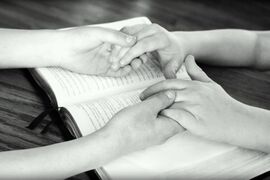 Zwei Menschen halten sich an den Händen, unter ihren Händen liegt eine Bibel