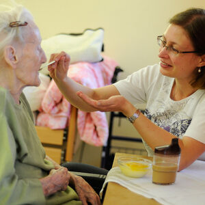 Pflegerin füttert Seniorin im