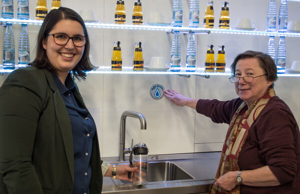 Sandra Alves (links) von der Mitarbeitenden-Vertretung im Bischöflichen Generalvikariat Hildesheim und Dommuseums-Direktorin Dr. Claudia Höhl weihten die Refill-Zapstelle im Domfoyer ein. Ein Aufkleber weist auf die Möglichkeit hin, sich mit Trinkwasser zu versorgen.