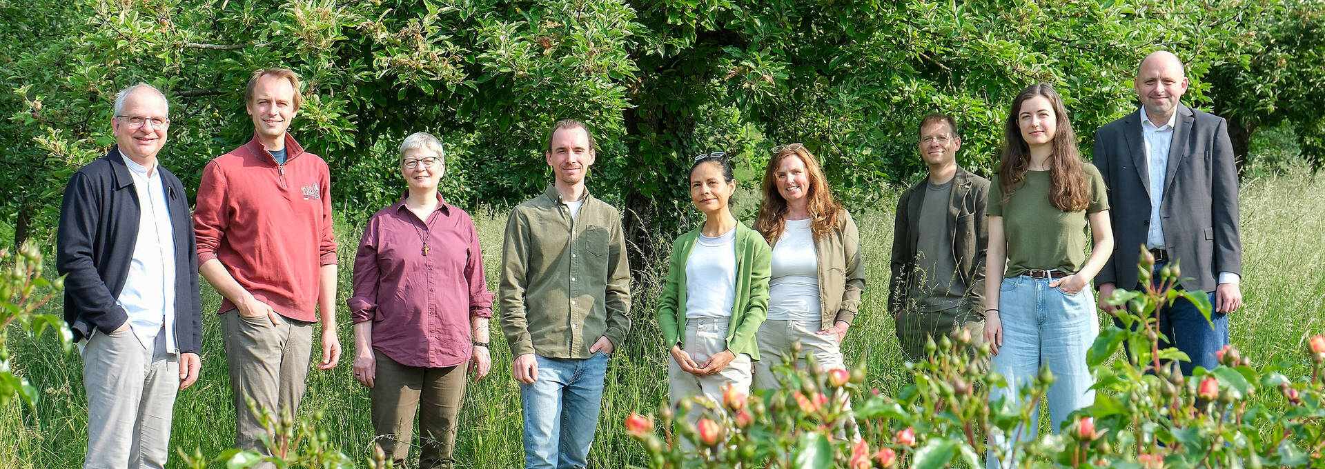 Foto des Umweltteams inmitten eines Gartens mit Rosen im Vordergrund, Bäumen und einer alten Mauer im Hintergrund