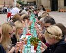 Menschen essen zusammen an einer langen Tafel auf dem Domhof bei einer Veranstaltung der Caritas.