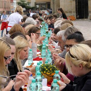 Menschen essen zusammen an einer langen Tafel auf dem Domhof bei einer Veranstaltung der Caritas.