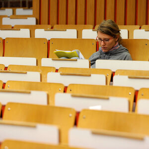Studentin sitzt vor Beginn einer Vorlesung in leerem Hörsaal
