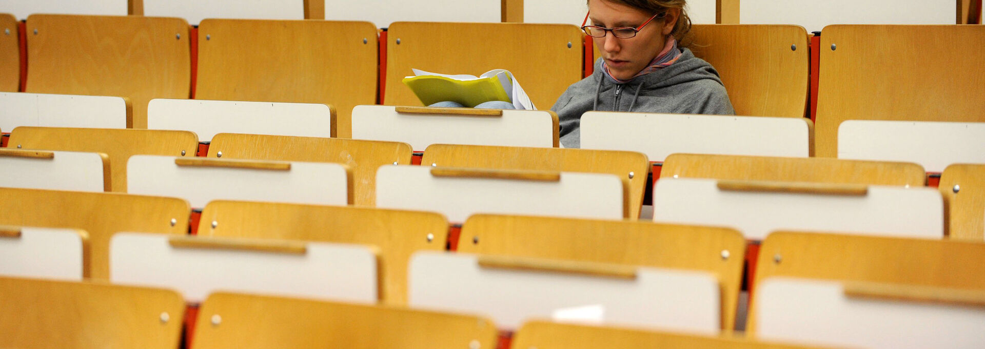 Studentin sitzt vor Beginn einer Vorlesung in leerem Hörsaal