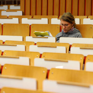 Studentin sitzt vor Beginn einer Vorlesung in leerem Hörsaal